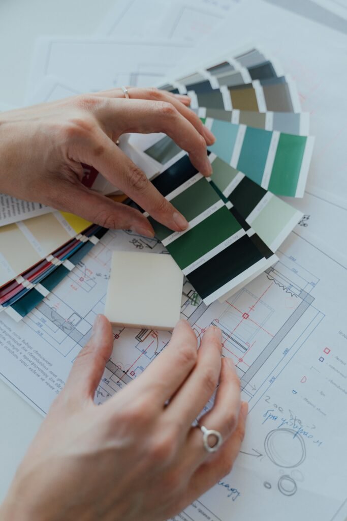 Sobre Construcción Jumilla Castril Granada - Jacobina Hands selecting color samples over architectural plans for interior design.